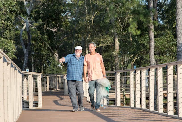 Men walking a boardwalk with fishing gear.