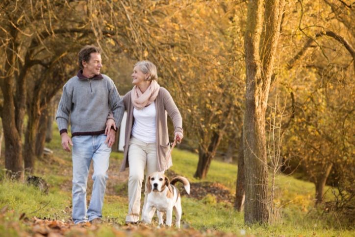 older couple walking a dog in woods